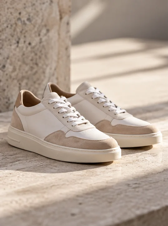 Crèmekleurige sneakers op een stenen ondergrond in warm zonlicht.