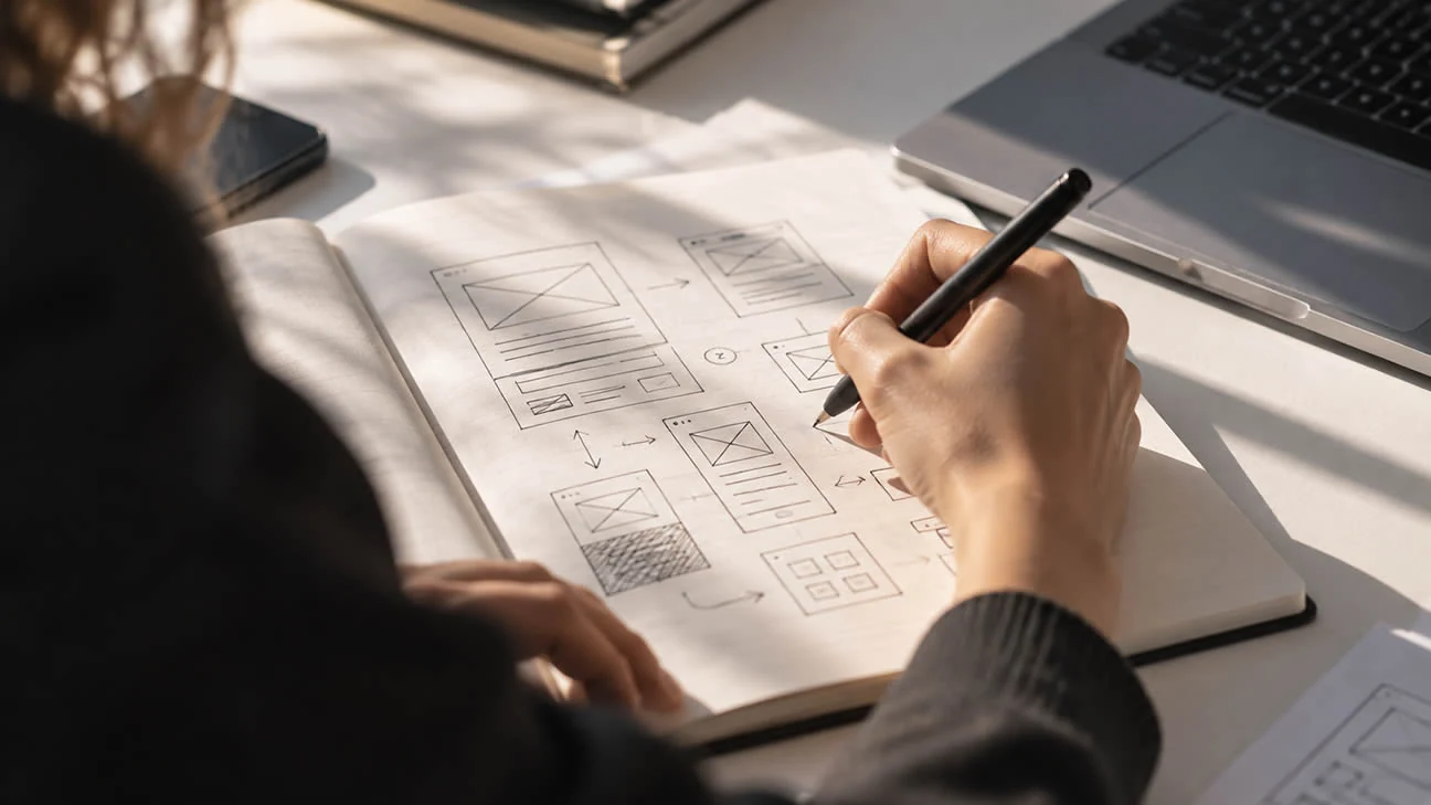 Een paginastructuur en wireframes worden met de hand uitgewerkt naast een laptop.
