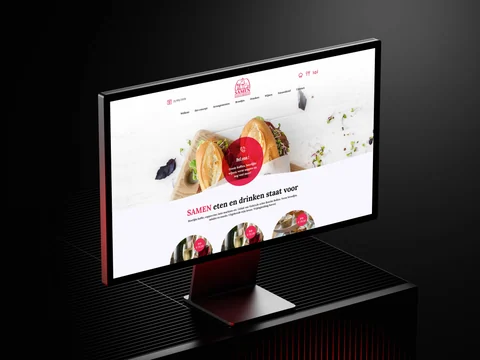 Desktopmonitor met de homepage van SAMEN Eten & Drinken op een zwart metalen bureau.