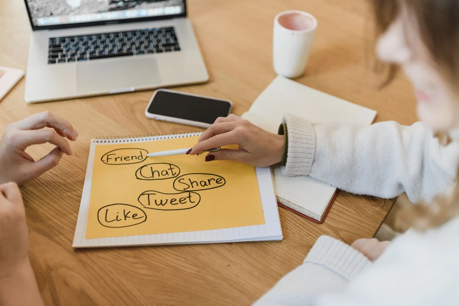 Handen bij een laptop, smartphone en notities voor een socialmediaplan.