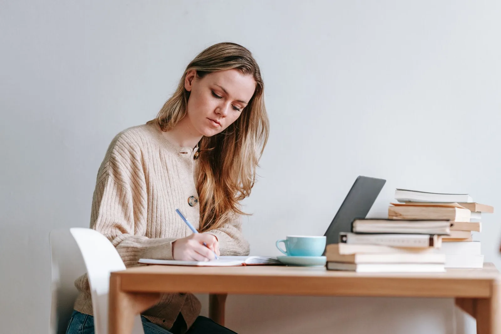 Een vrouw maakt aantekeningen naast haar laptop en boeken.