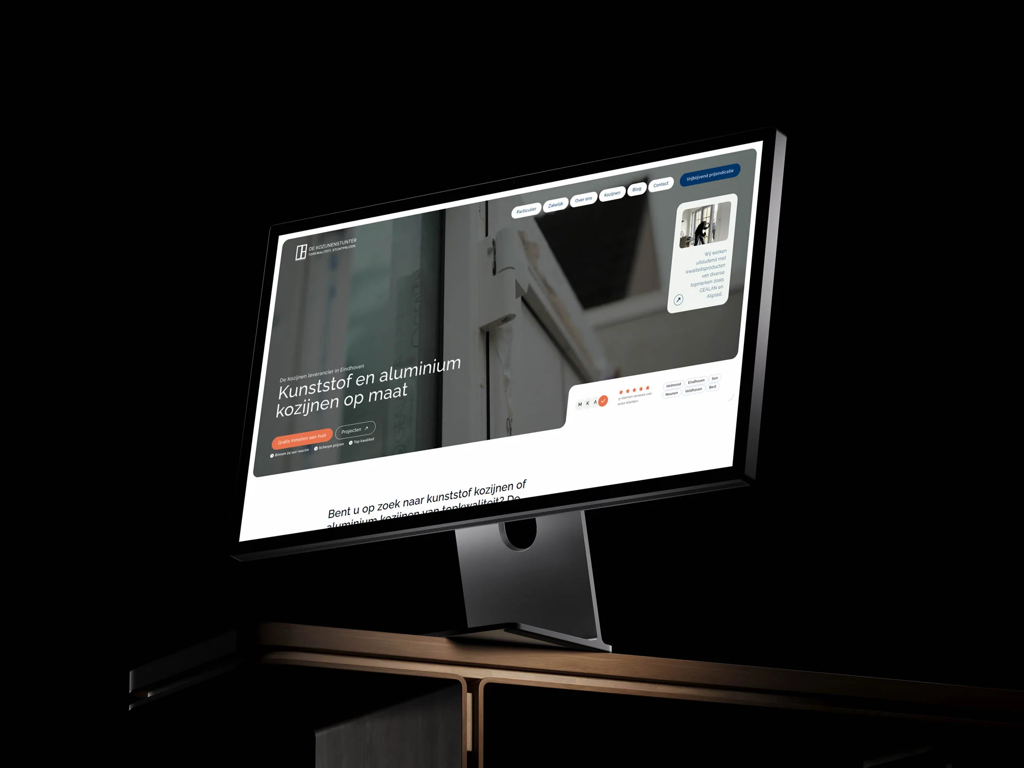 De Kozijnenstunter-homepage op een desktopmonitor boven een houten tafel.